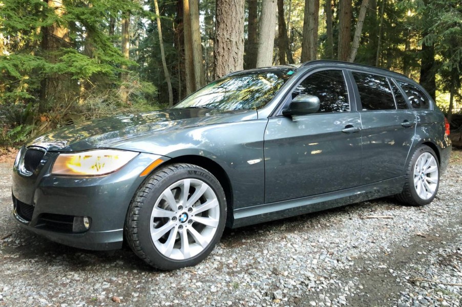 A dark-green 2011 BMW 328i Sports Wagon on a forest gravel path