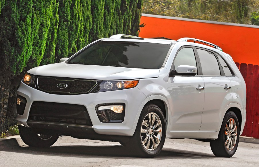 A white 2013 Kia Sorento parked near foliage and an orange building