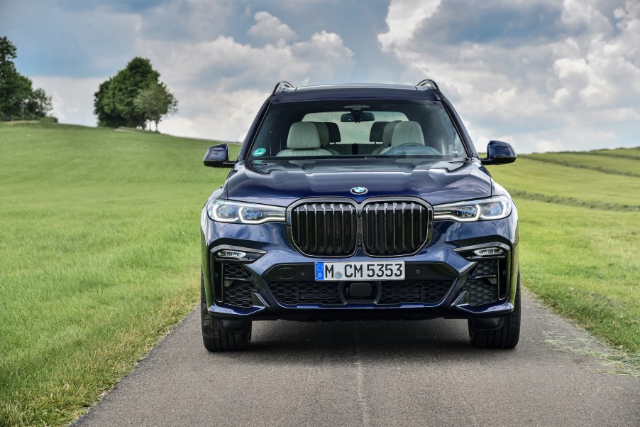 A dark-blue 2020 BMW X7 full-size crossover SUV parked on a narrow road passing through grassy hills