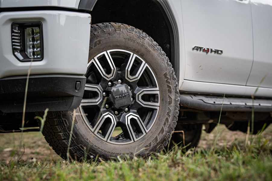 The driver's side door, tire, and front bumper of a white 2020 GMC Sierra HD AT4 pickup truck parked in the grass