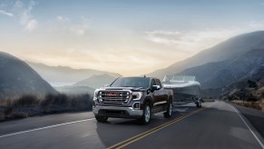 A black 2020 GMC Sierra SLT tows a boat on a two-lane mountain road