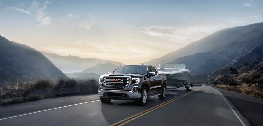 A black 2020 GMC Sierra SLT tows a boat on a two-lane mountain road