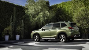 A green 2020 Subaru Forester parked on a patterned concrete slab surrounded by potted trees and shrubbery