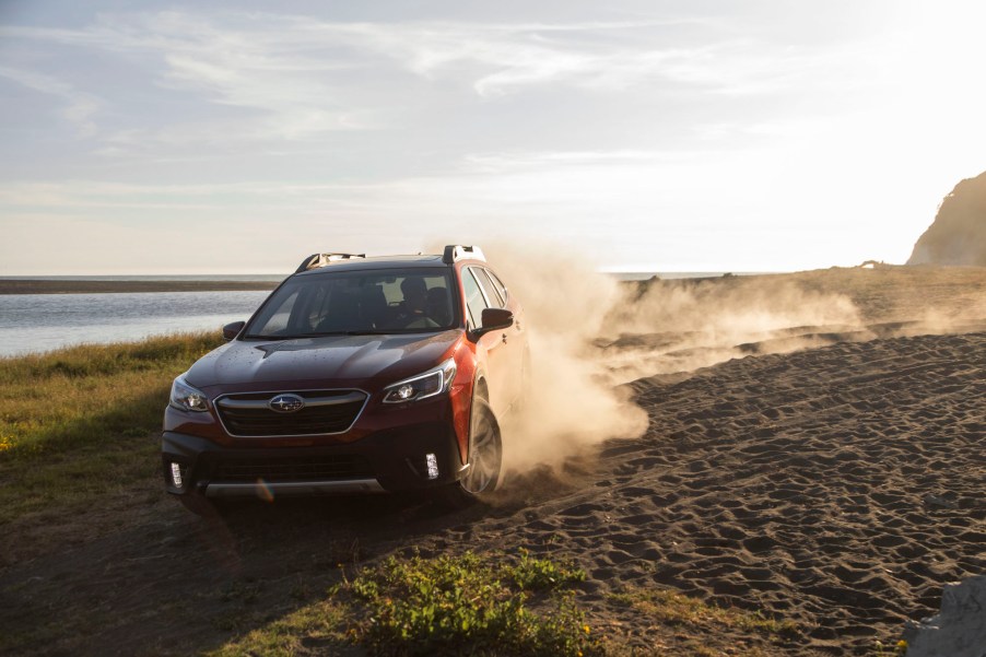 A red 2020 Subaru Outback kicks up sand as it drives on a beach