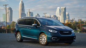 A 2021 Chrysler Pacifica Pinnacle Hybrid, shown in Fathom Blue, parked on asphalt in front of a cityscape