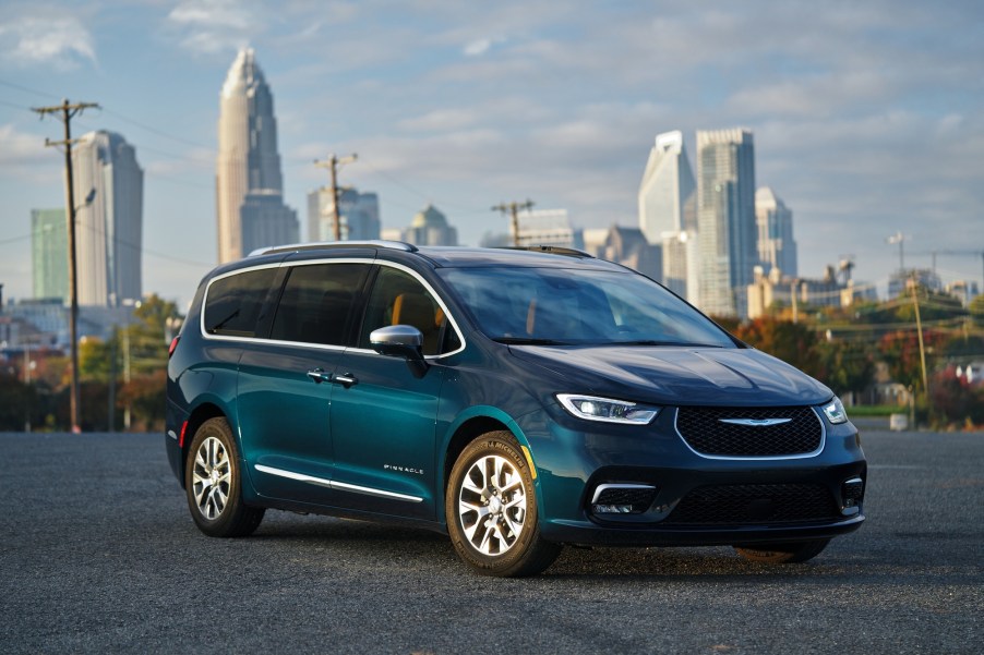 A 2021 Chrysler Pacifica Pinnacle Hybrid, shown in Fathom Blue, parked on asphalt in front of a cityscape