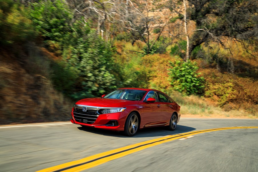 A red 2021 Honda Accord Hybrid travels on a two-lane highway on a hillside