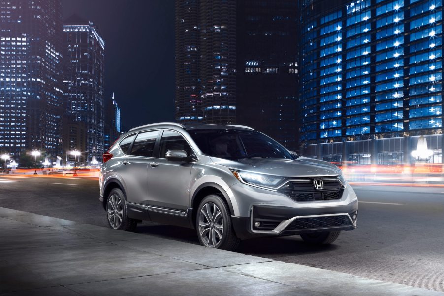 A silver 2021 Honda CR-V Touring model with its headlights on while parked on a city street at night