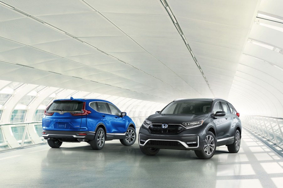 Two 2021 Honda CR-V Touring models, one blue and one dark gray, parked next to each other on a white covered bridge