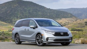 A silver 2021 Honda Odyssey minivan parked in front of grassy hills