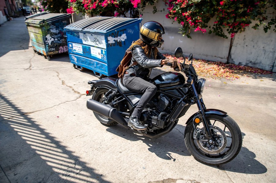 A rider takes a black 2021 Honda Rebel 1100 through an alley