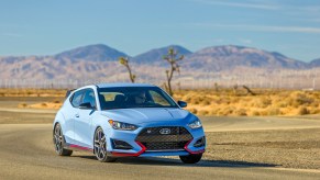 A sky-blue 2021 Hyundai Veloster N sports car travels on a winding road course in a desert