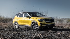 A yellow 2021 Kia Seltos all-wheel-drive compact SUV drives through the mud on a sunny day