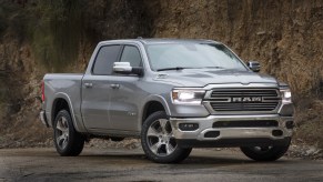 A silver 2021 Ram 1500 Laramie pickup truck parked on wet asphalt at the foot of a cliff