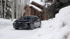 A dark-blue 2021 Toyota Avalon Limited AWD parked in the snow outside a modern cabin in the woods