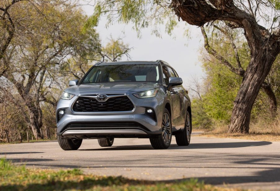 A silver all-wheel-drive 2021 Toyota Highlander Platinum model parked on a rural road amid trees and shrubs