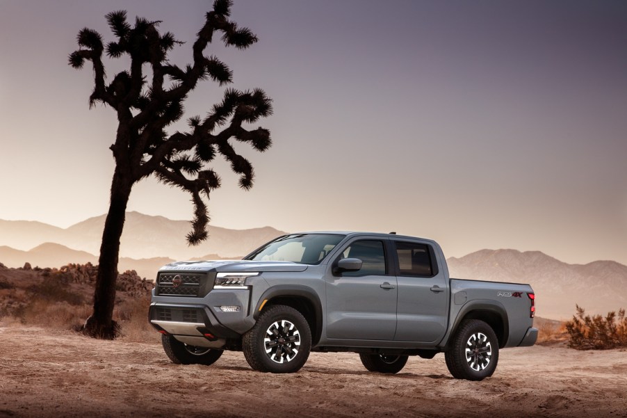 A light gray 2022 Nissan Frontier sits beside a tree among a rugged dessert