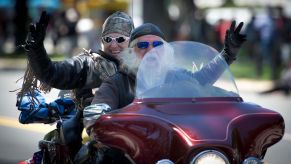 A motorcycle rider and passenger wave from a maroon Harley-Davidson