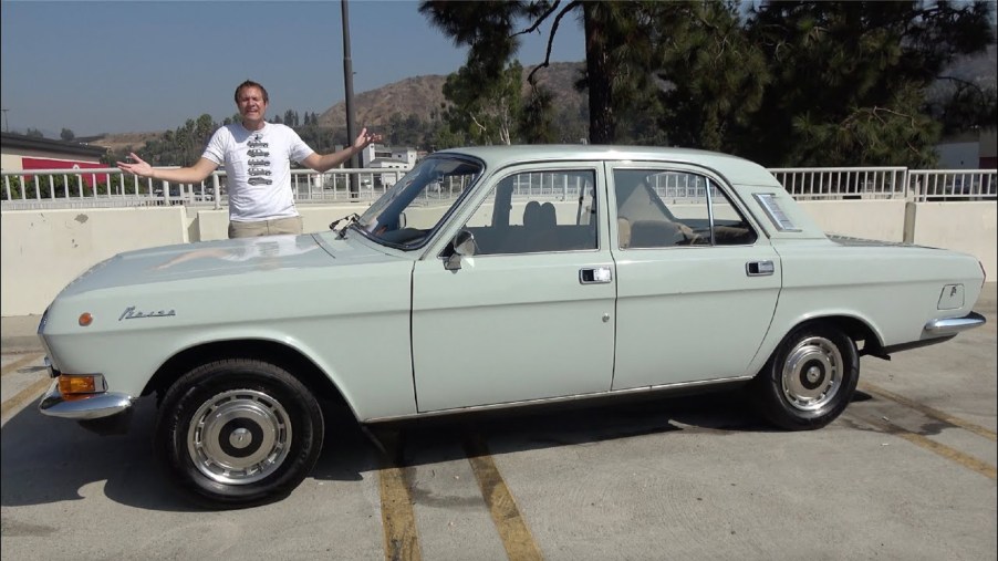 Doug DeMuro with a gray 1988 Volga GAZ-24-10 on a parking garage roof