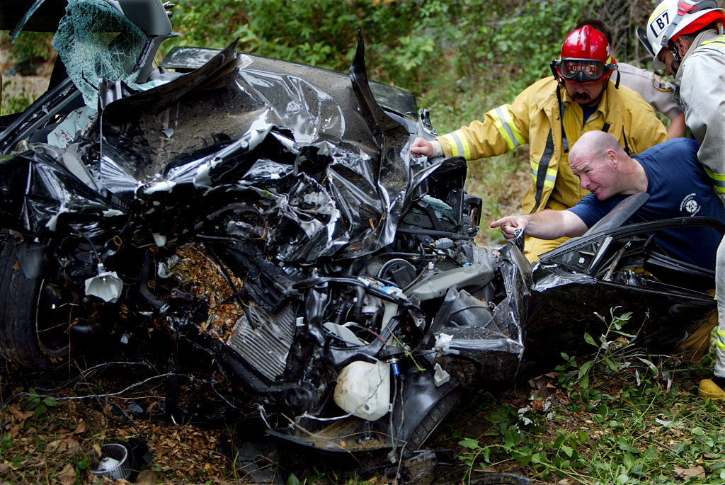 Mangled remains of car with firemen looking on