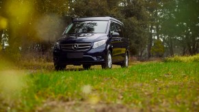 A navy-blue Mercedes-Benz Metris Weekender camper van parked on grass next to trees