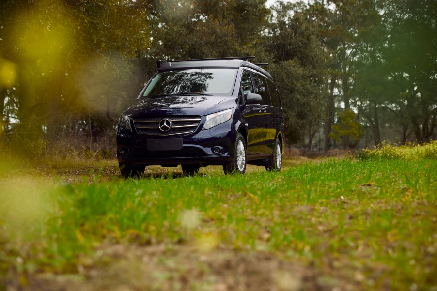 A navy-blue Mercedes-Benz Metris Weekender camper van parked on grass next to trees