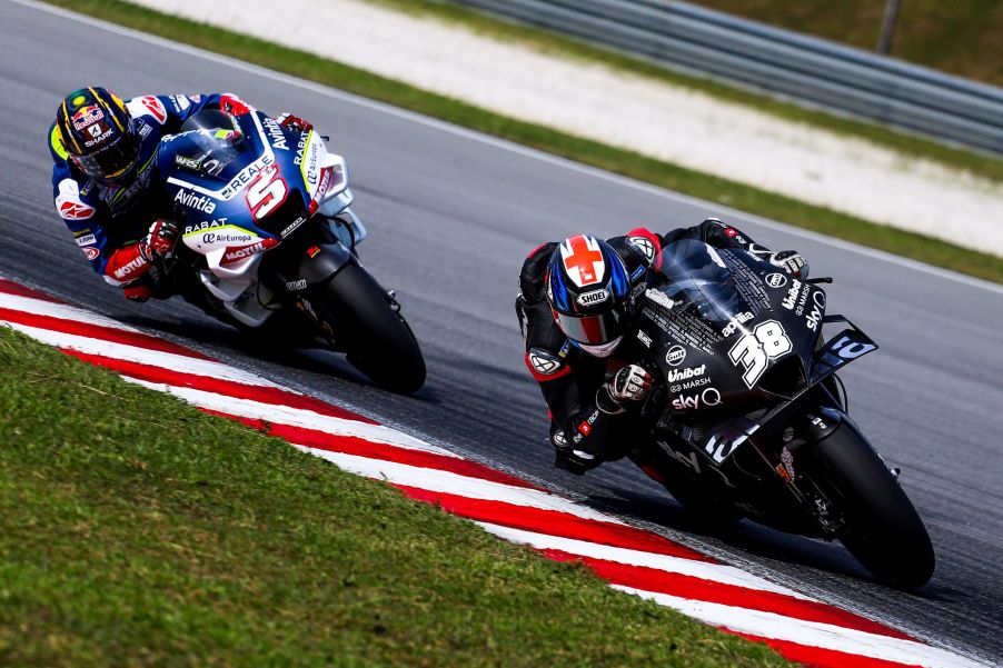 MotoGP riders Bradley Smith on a black-and-white bike and Johann Zarco on a white-and-blue bike countersteer their motorcycles around a corner