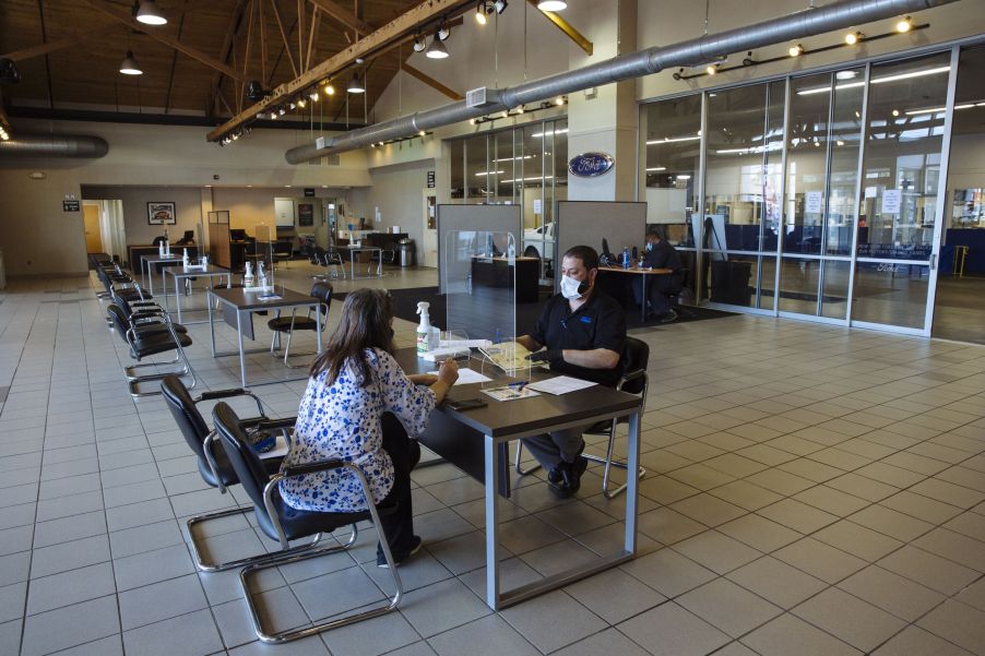 A customer and a salesperson sit behind plastic COVID-19 barriers in a New Jersey Ford and Kia car dealer