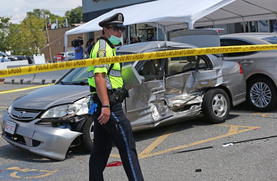 A police officer walks past one of several damaged vehicles after a car accident in a parking lot. A car crashed into the Bellagio Nails & Spa in Medford, Massachusetts, on July 28, 2020, with people inside and hitting several cars.