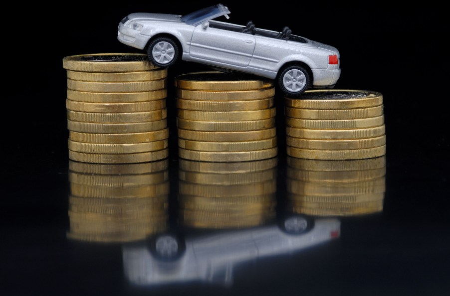 A silver Audi convertible model car rests atop three stacks of coins