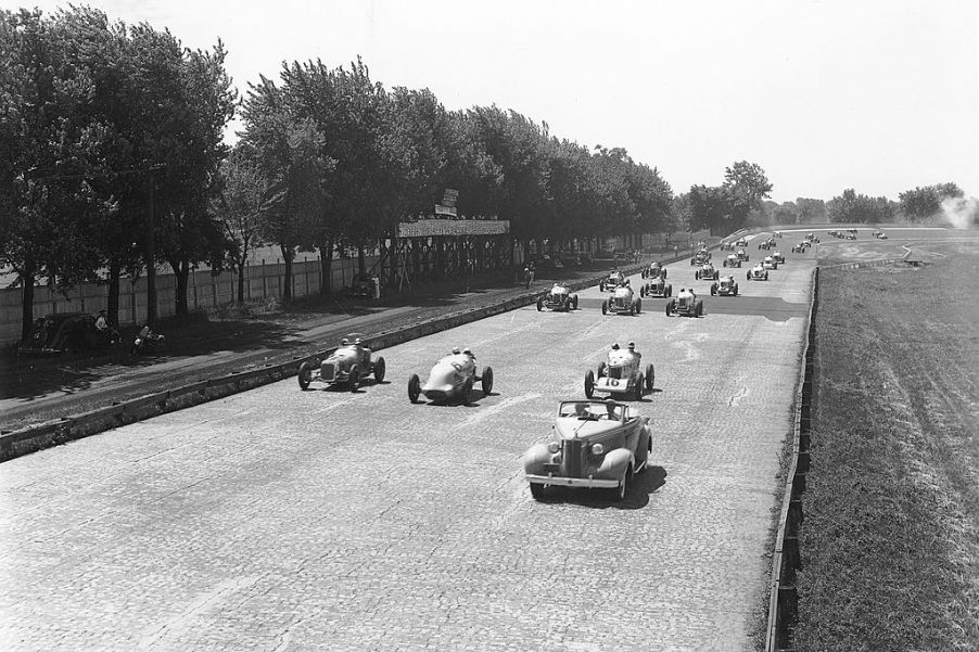 Indy cars driving on the brick racing surface of the Indianapolis Motor Speedway during the pace lap for the Indianapolis 500 in 1937