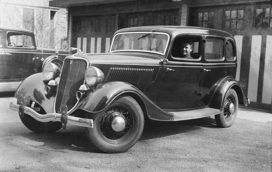 Black and white photo of a man driving a 1934 Ford Fordor, historically used as a getaway car