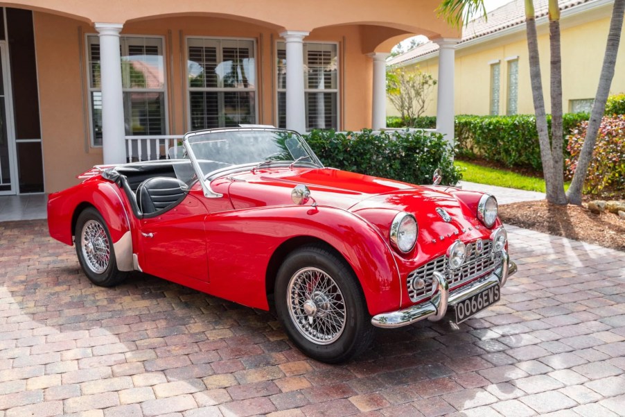 A red TR3A-spec 1960 Triumph TR3 by a peach-colored house