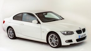 A white 2011 BMW 3 Series coupe in a white studio