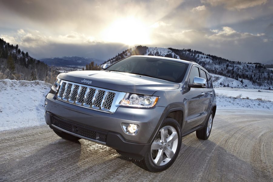 A grey 2011 Jeep Grand Cherokee driving down a road with a setting sun in the background