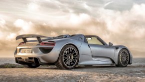 A low-angle rear 3/4 view of a silver 2015 Porsche 918 Spyder on a sandy beach