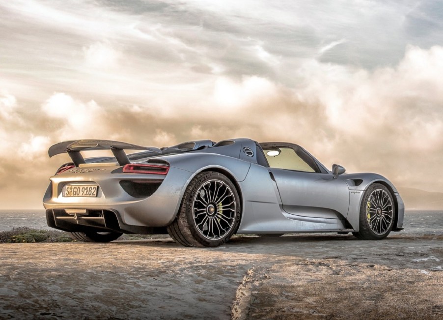 A low-angle rear 3/4 view of a silver 2015 Porsche 918 Spyder on a sandy beach