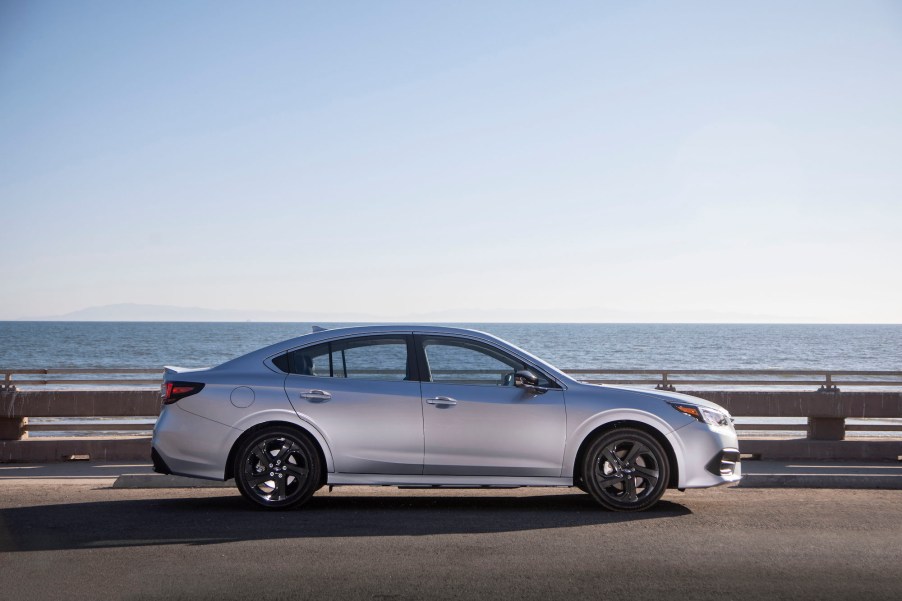 A silver 2020 Subaru Legacy Sport midsize sedan parked on the pavement in front of a large body of water on a cloudless day