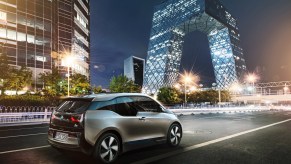 A silver 2021 BMW i3 compact electric car on a city road in front of modern glass buildings