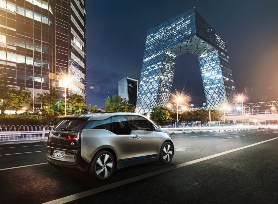 A silver 2021 BMW i3 compact electric car on a city road in front of modern glass buildings