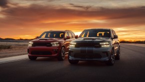 A red 2021 Dodge Durango R/T Tow N Go SUV (left) and a white-and-blue Durango SRT Hellcat SUV parked side-by-side on a racetrack at sunset