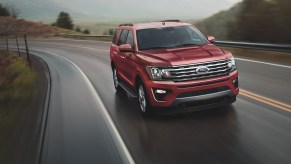 A red 2021 Ford Expedition full-size SUV travels on a two-lane highway up a mountain on a foggy day