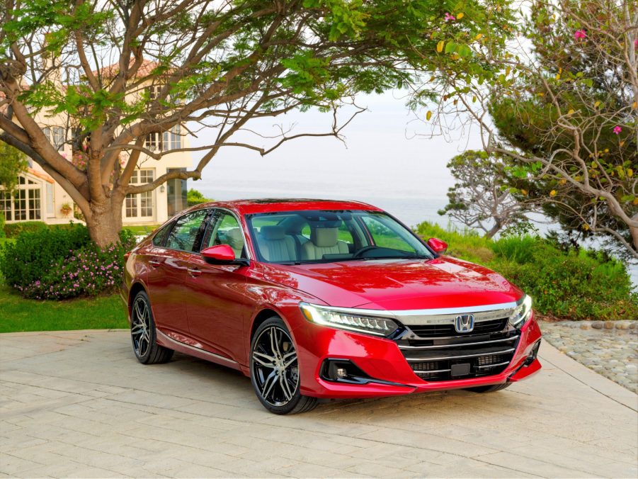 A red 2021 Honda Accord Hybrid parked in a driveway with trees surrounding it