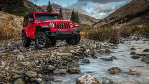 An orange 2021 Jeep Wrangler Rubicon parked on rocky terrain next to a river