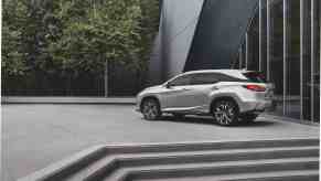 A silver 2021 Lexus RX L midsize luxury SUV parked at the top of some concrete steps next to a modern building and trees