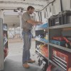 A man stands inside a white 2021 Nissan NV cargo van lined with shelves of tool chests and other work equipment