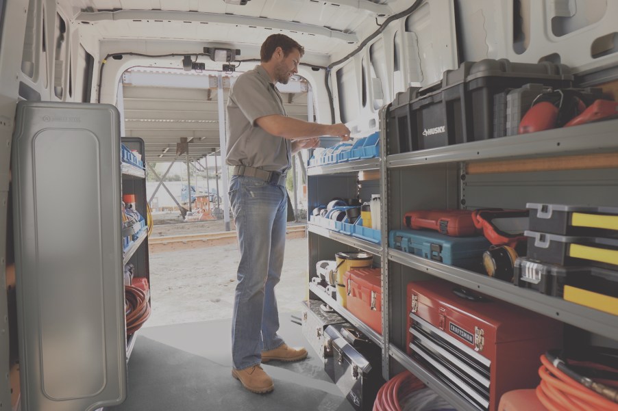 A man stands inside a white 2021 Nissan NV cargo van lined with shelves of tool chests and other work equipment