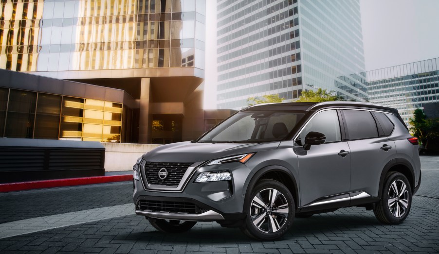 A dark-gray metallic 2021 Nissan Rogue compact crossover SUV parked outside glass skyscrapers