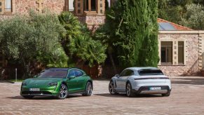 A green 2021 Porsche Taycan Turbo S Cross Turismo next to a rear-facing white Taycan 4S Cross Turismo by a villa