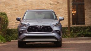 A silver 2021 Toyota Highlander midsize crossover SUV parked in the red-brick driveway of a tan-brick building